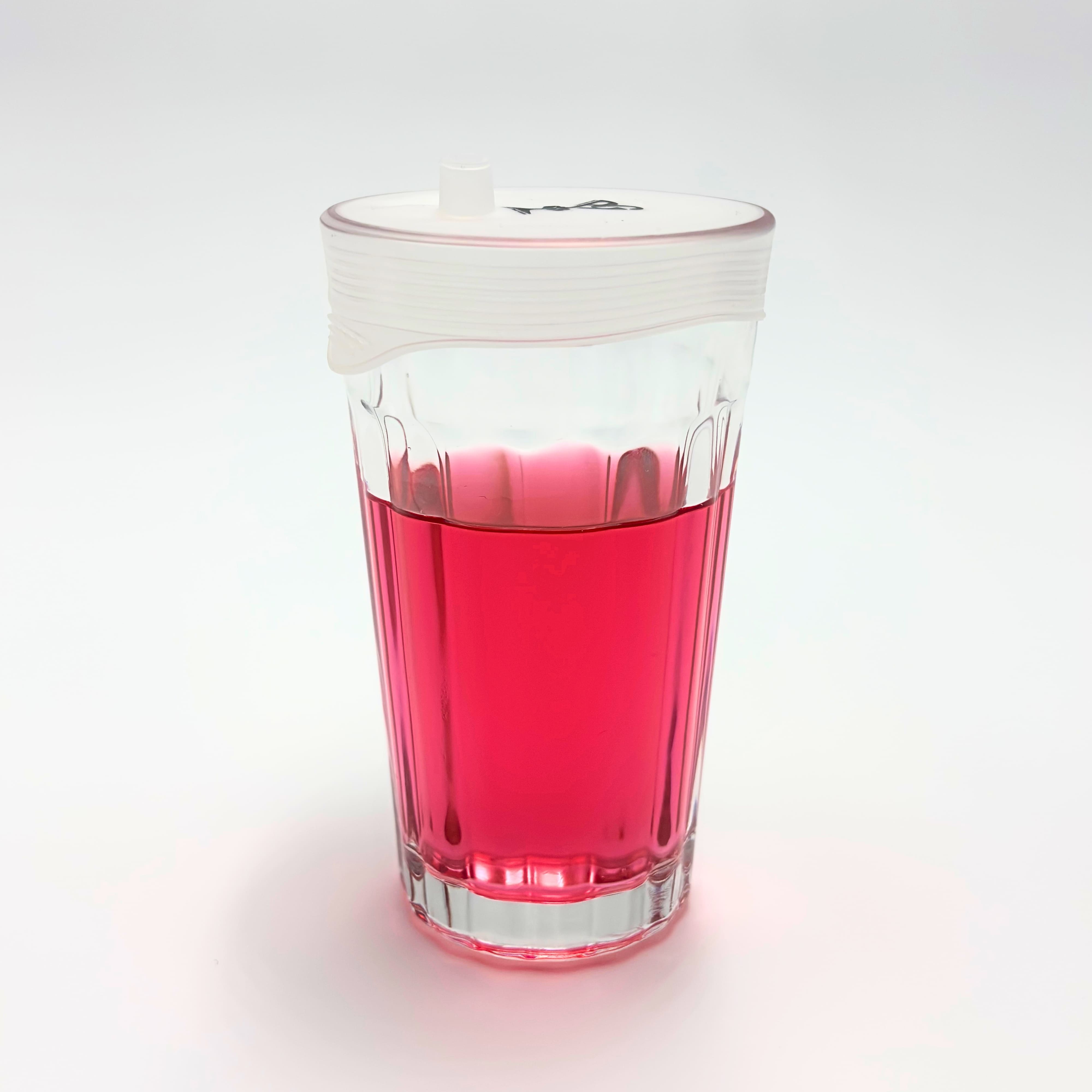 Capote de verre en silicone avec tétine Protect Your Glass sur un verre contenant une boisson rose.